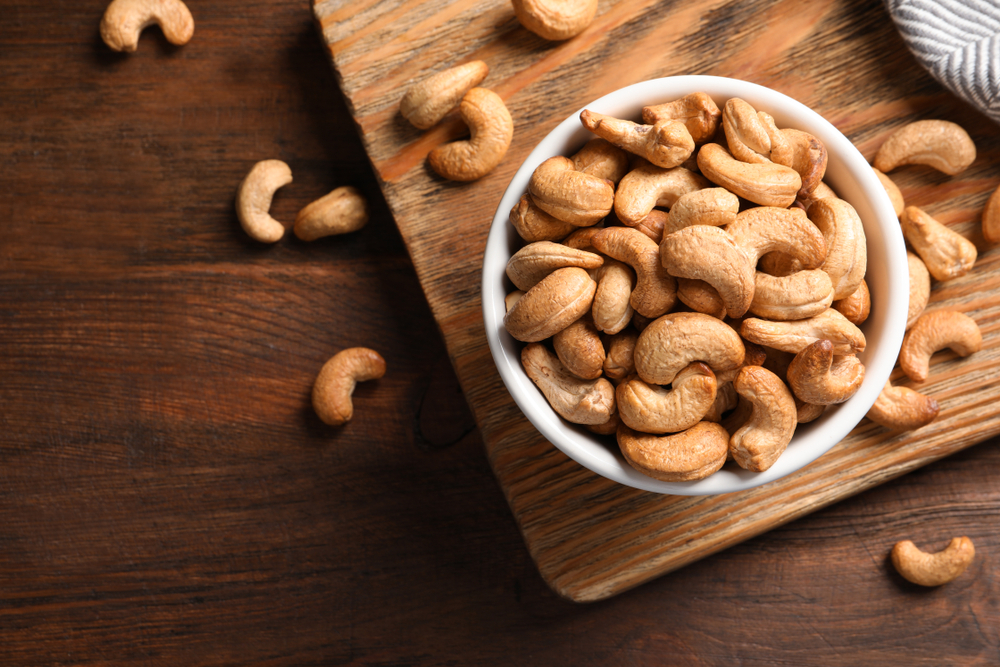 Tasty cashew nuts in bowl on wooden table, top view